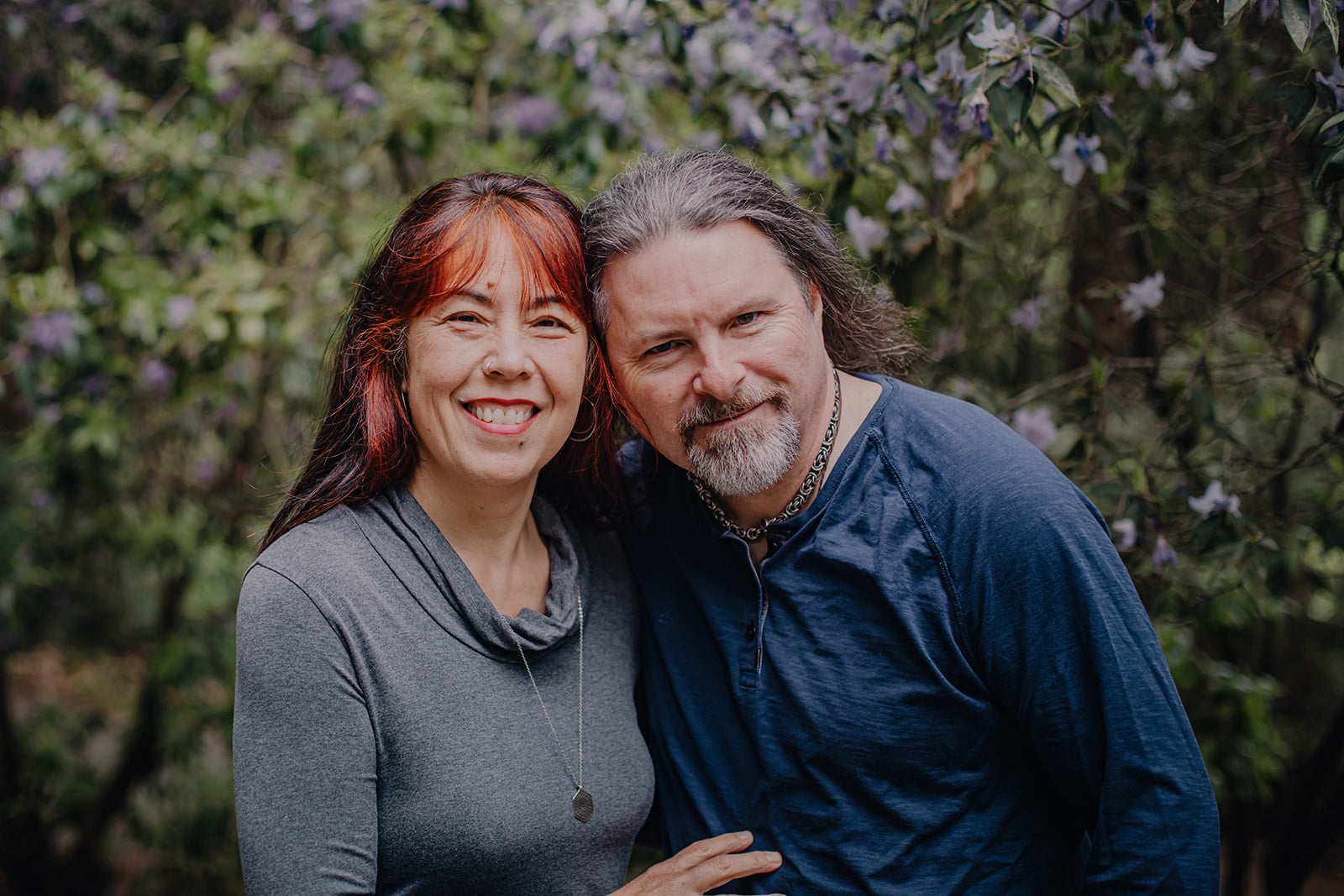 Two people standing together in front of a blurred natural background